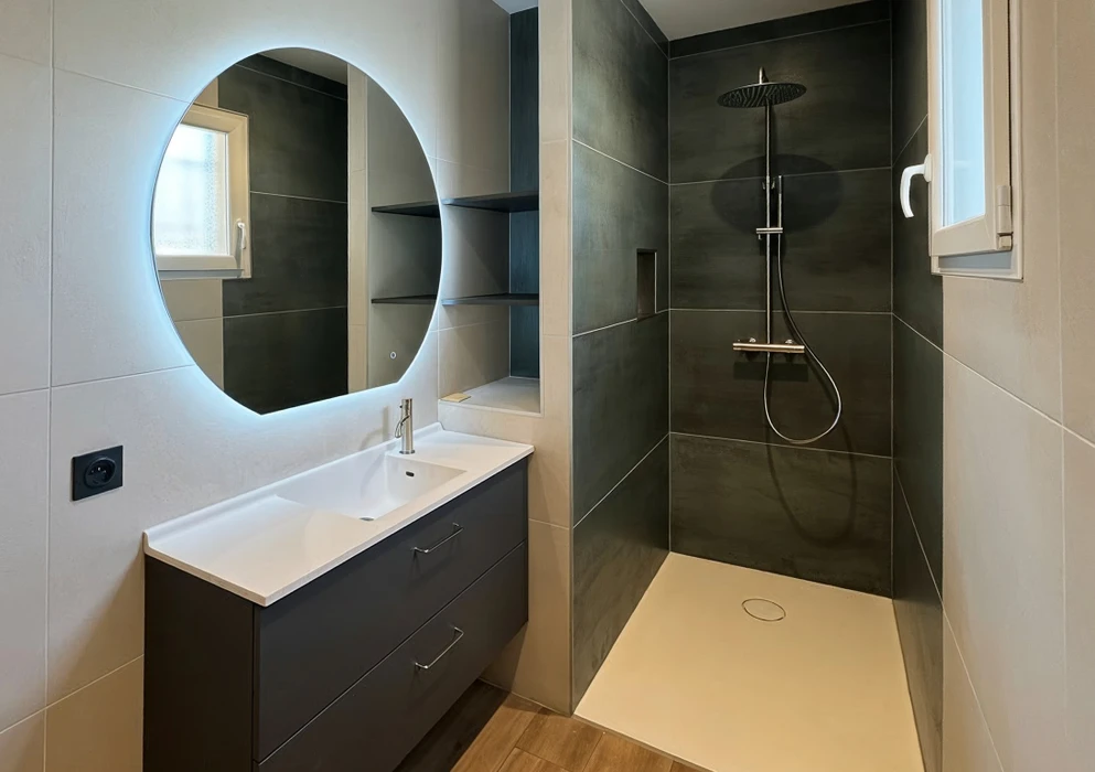 Salle de bain moderne avec douche à l'italienne ouverte, carrelage noir mat dans l'espace douche contrastant avec carrelage beige clair sur les murs