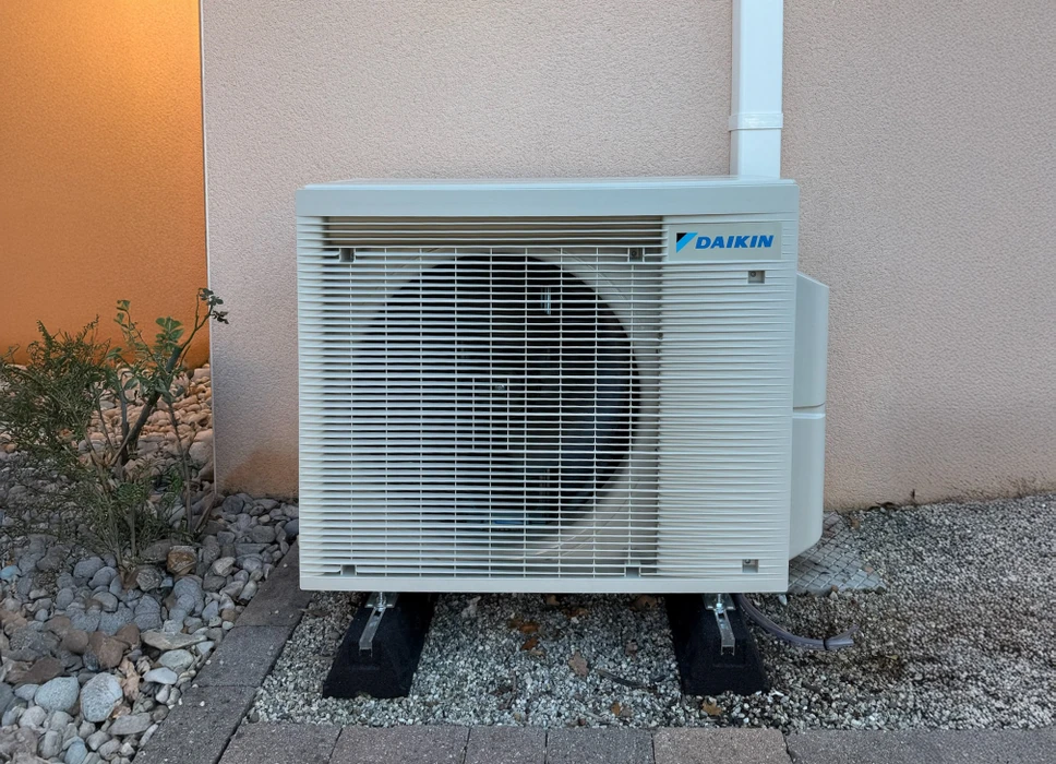 Unité extérieure de climatisation Daikin installée sur dalle béton contre mur crépi beige et orange