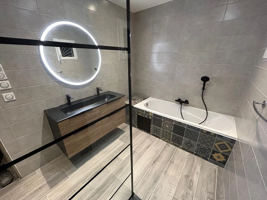 Salle de bain moderne avec baignoire encastrée, paroi de douche en verre, vasque noire sur meuble suspendu en bois