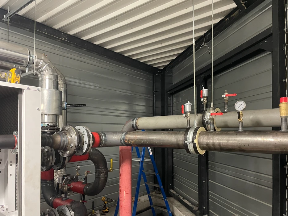 Salle technique industrielle avec tuyauterie grise isolée, vannes de régulation et équipements de chauffage ou climatisation